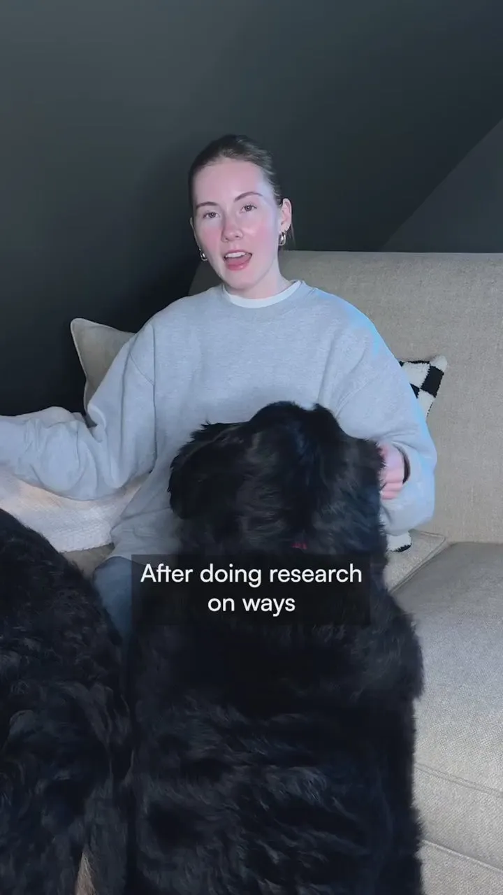 A woman in a grey sweatshirt on her sofa with her fluffy black dog, talking to camera