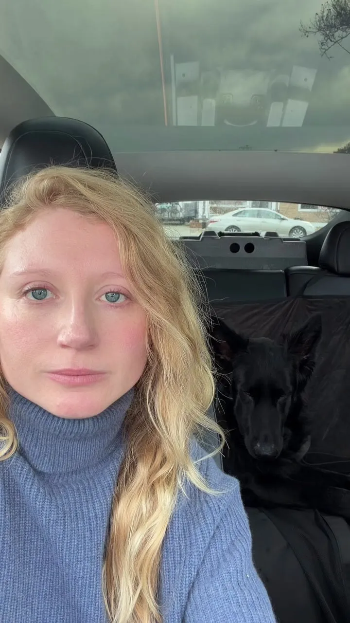 A customer in her car with her black German Shepherd resting on the back seat