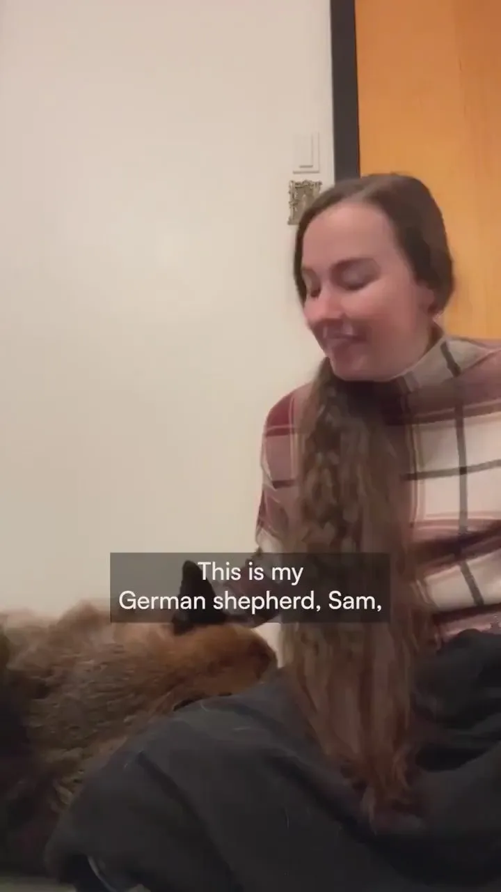 A woman in a plaid scarf sitting on the floor beside her German shepherd, Sam
