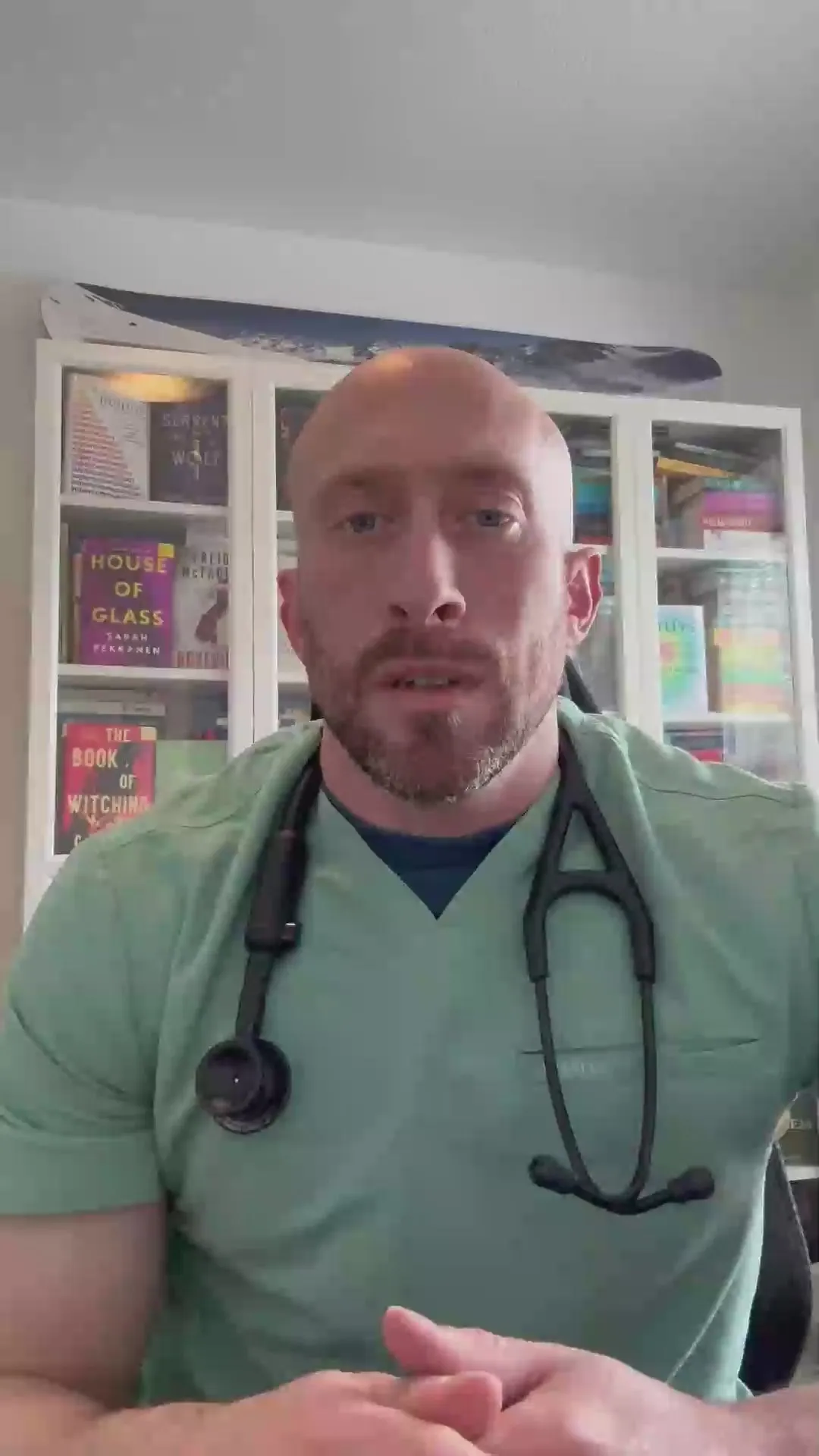 A veterinarian in green scrubs and a stethoscope talking to camera in front of a bookshelf