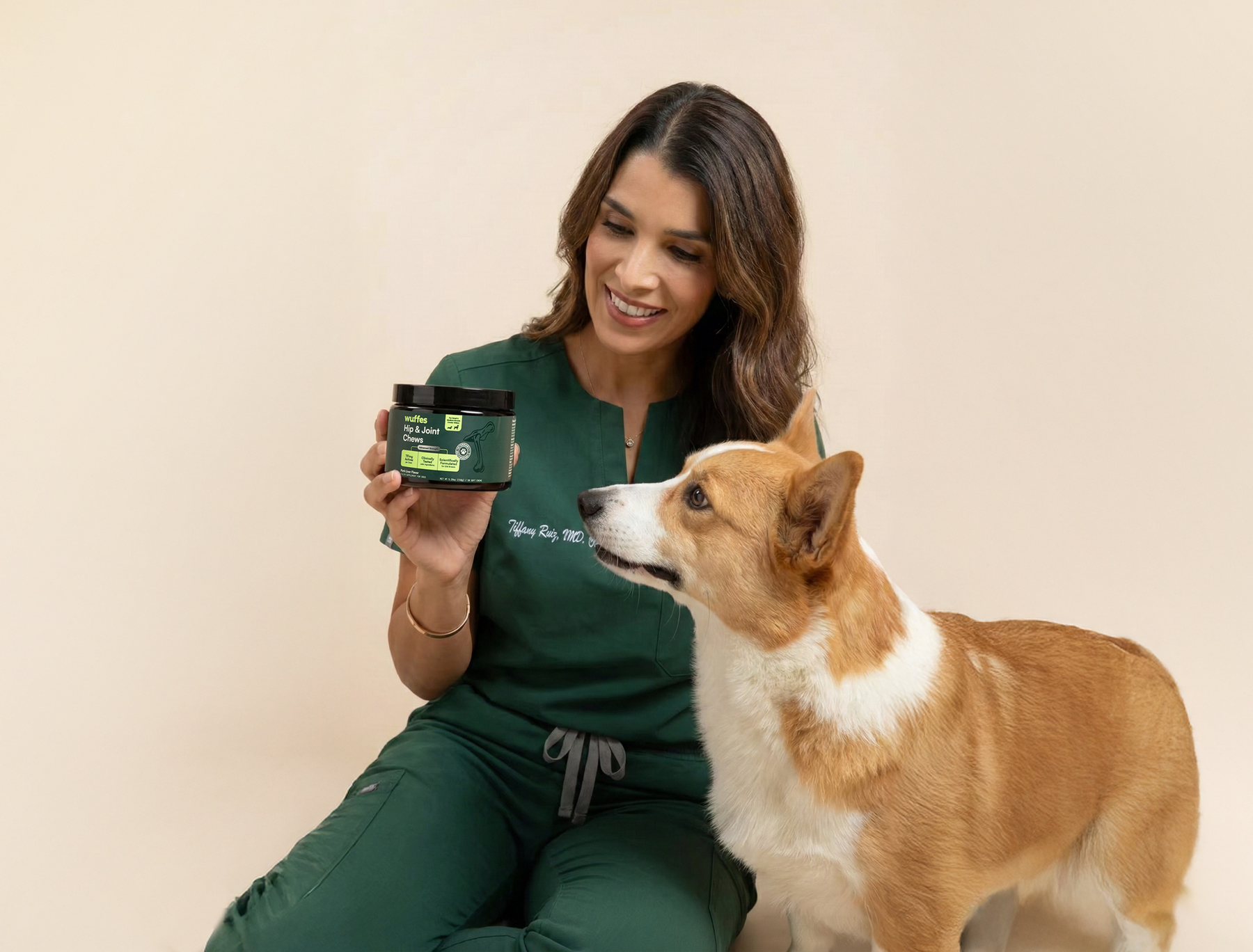 Woman in green scrubs holding a jar showing a dog joint supplement next to a brown and white dog